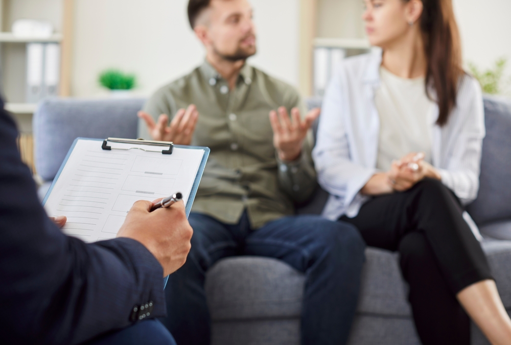 couple man and woman sitting on sofa in counselor's office during family therapy session